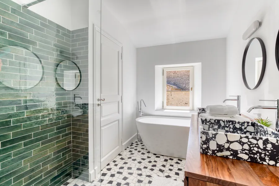 A bathroom with glazed green tiles, a freestanding tub and terrazzo basins