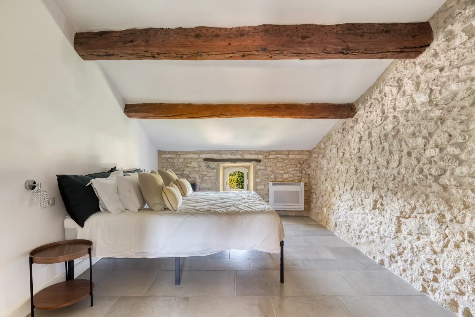 A calm bedroom with old oak beams and a long stone wall