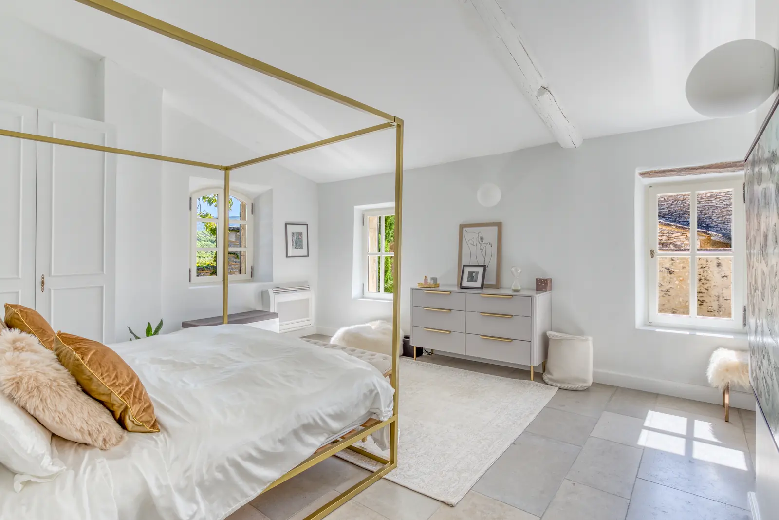 A bedroom with a brushed-gold four-poster bed and white linens