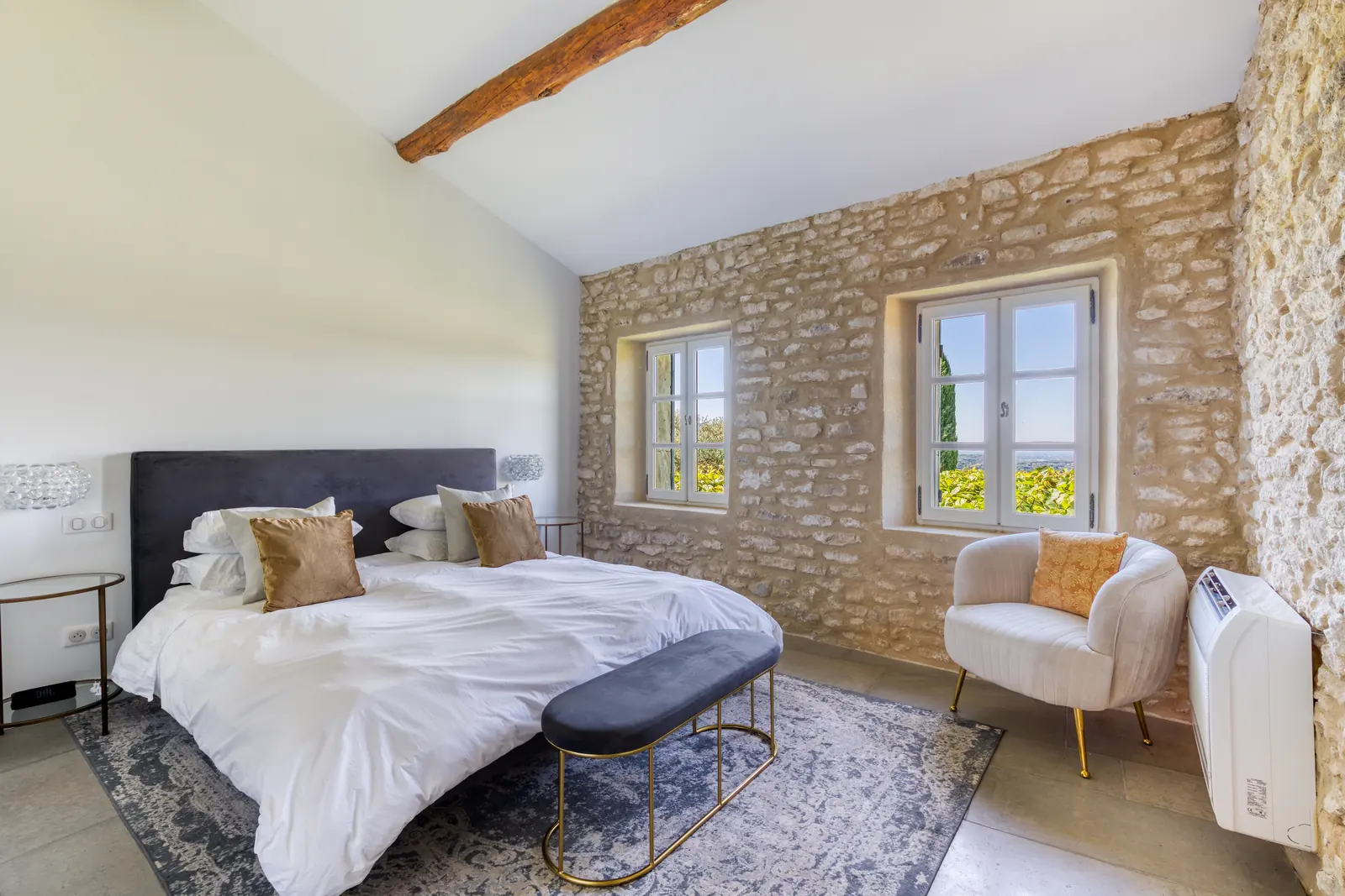 A bedroom with an exposed stone wall, beamed ceiling and a view of the vineyards