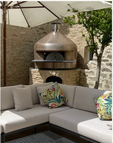 A copper wood-fired pizza oven set into the stone courtyard wall