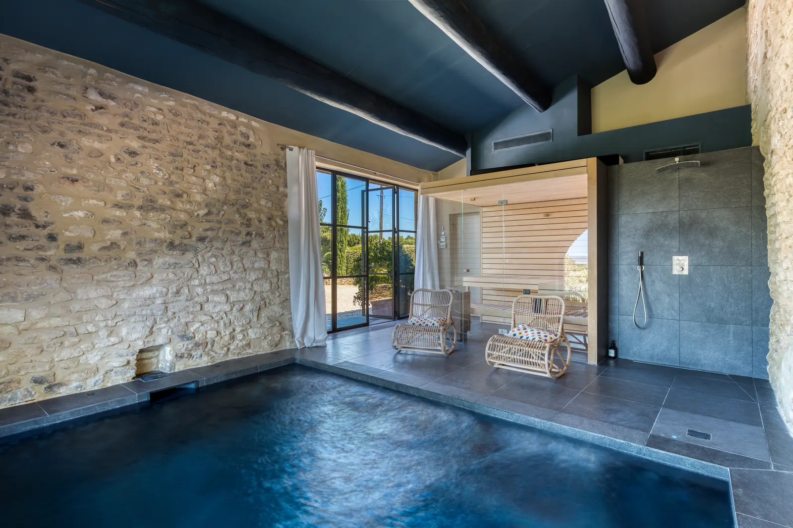 The indoor heated pool between stone walls, with the sauna and rain shower beyond